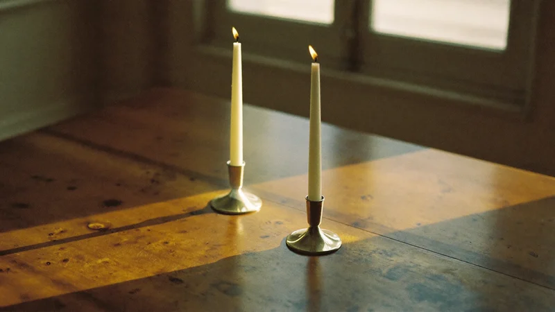 Deux chandelles allumées dans des bougeoirs en laiton sur une table sombre